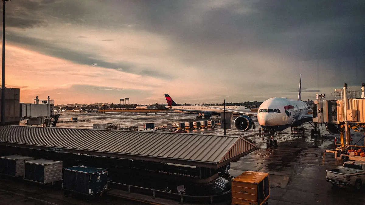 Passenger jet parked at an airport gate under a dramatic dawn sky, with service vehicles on the apron