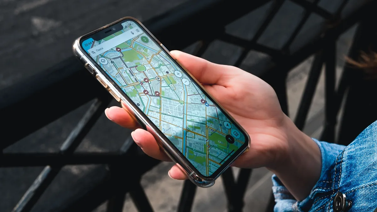 Hand holding a smartphone showing a street map app, the kind of dropped pin families share to fix a meeting point