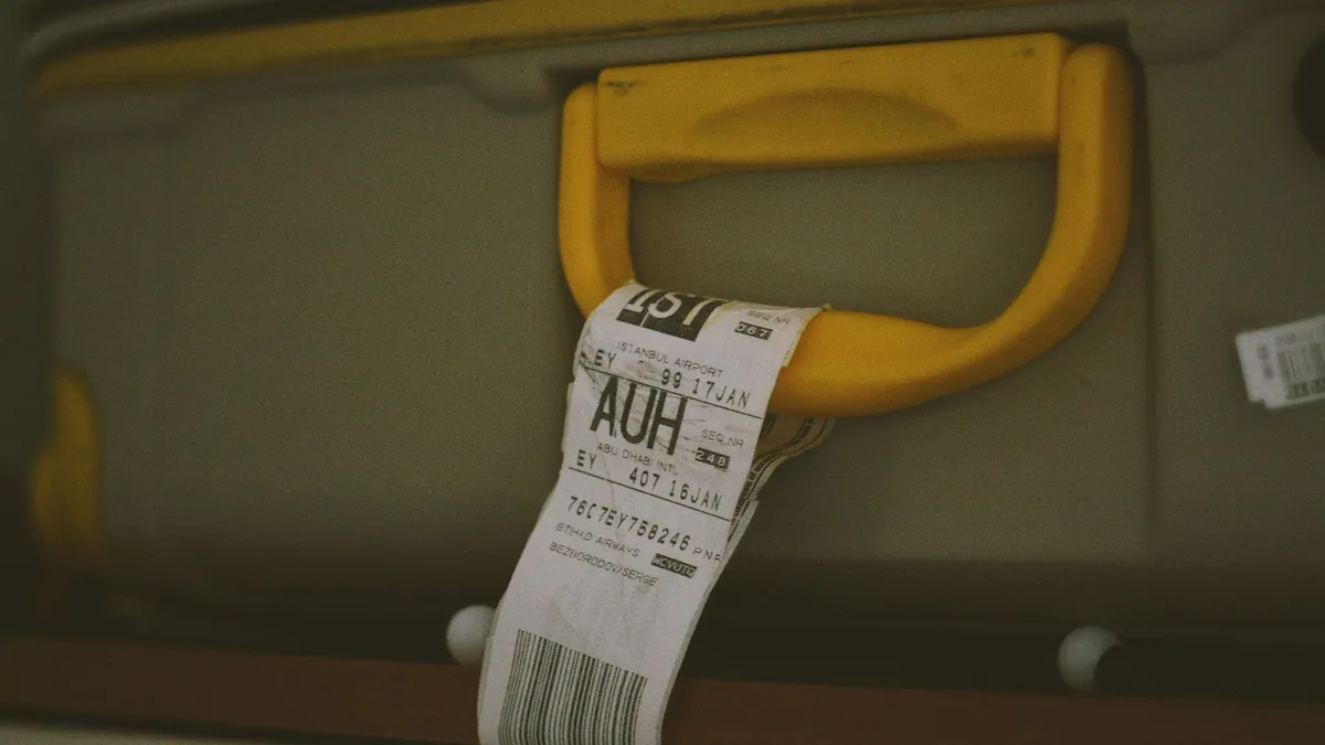 Close-up of a yellow suitcase handle carrying a printed airline baggage tag with a barcode and routing code