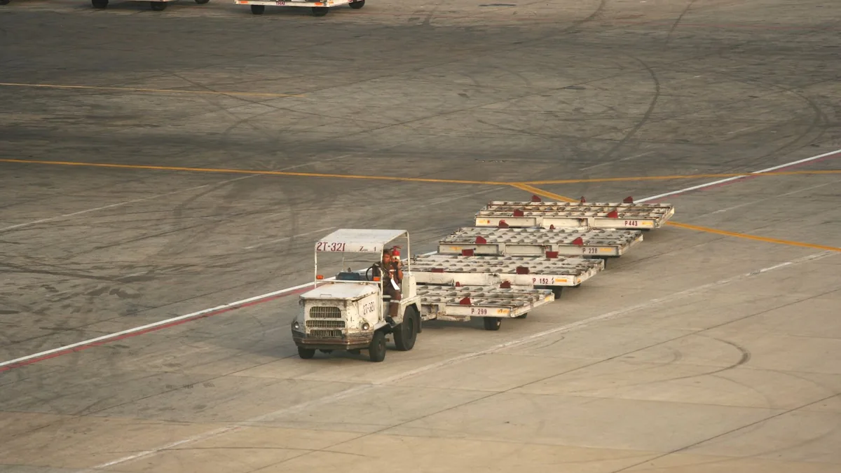 Baggage tug pulling a line of empty luggage dollies across an airport apron in warm evening light
