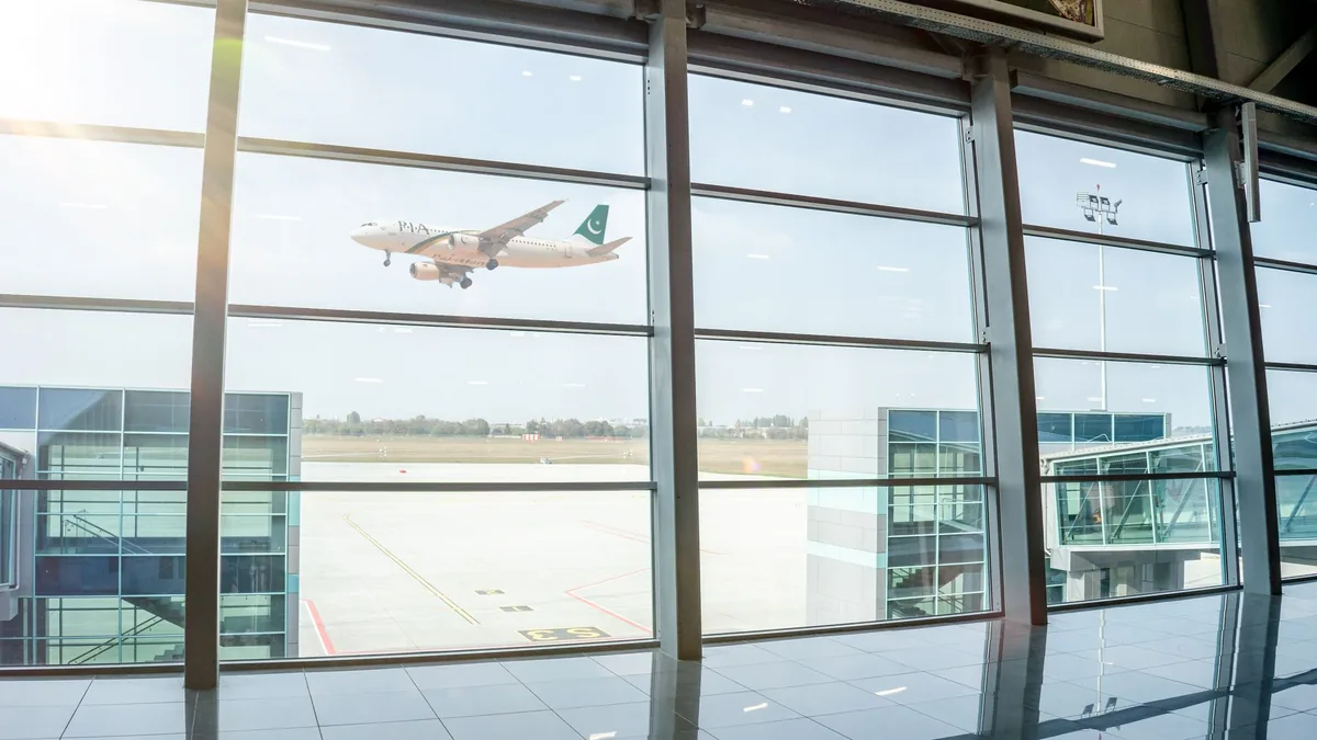 Airliner coming in to land, seen through the tall glass windows of an airport terminal on a bright day