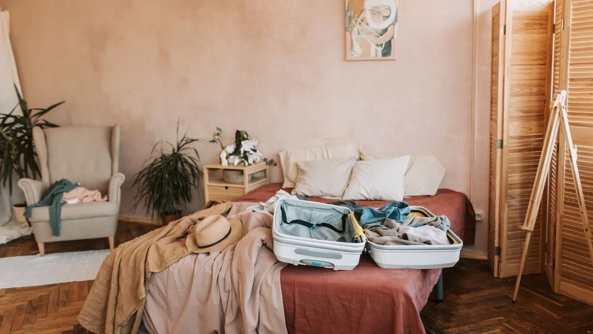 Two open suitcases with clothes on an unmade bed in a warm, softly lit bedroom, a rest stop before the onward journey