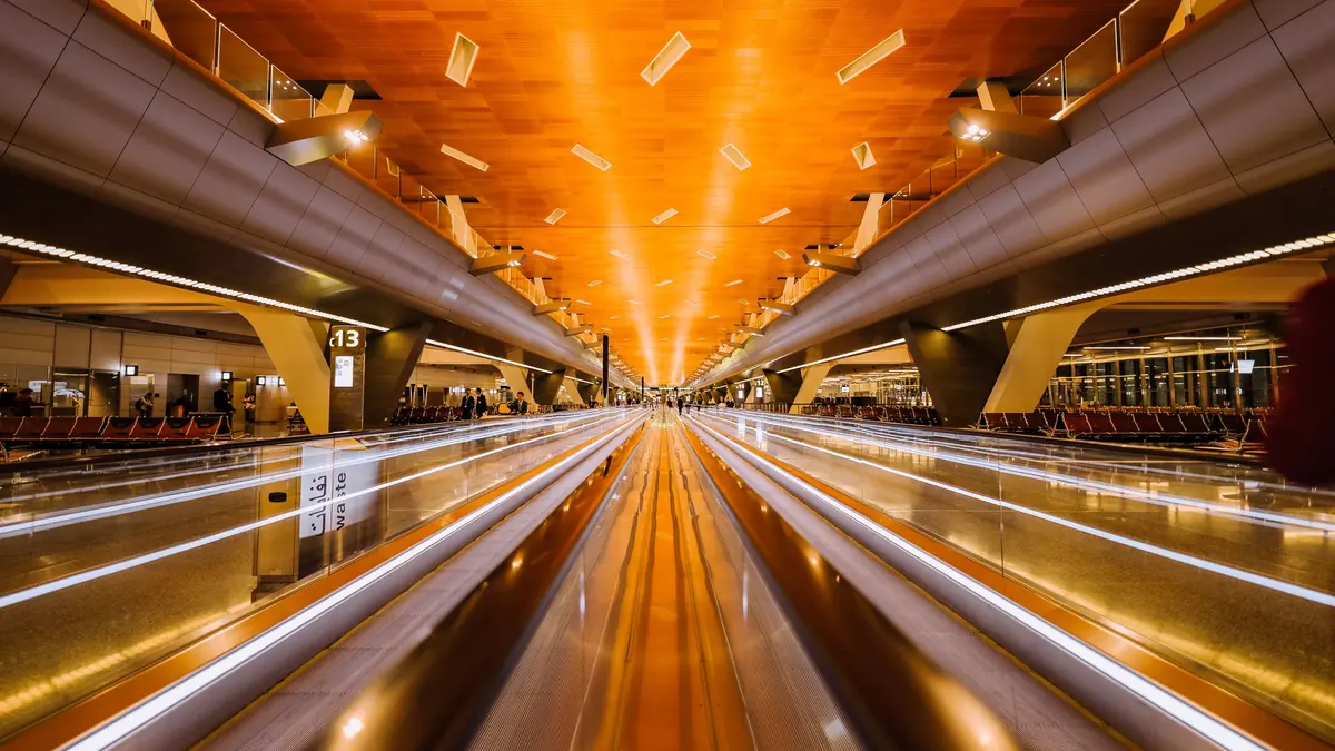 Long-exposure view of an empty airport moving walkway under a warm orange-lit ceiling, lines of light streaking ahead