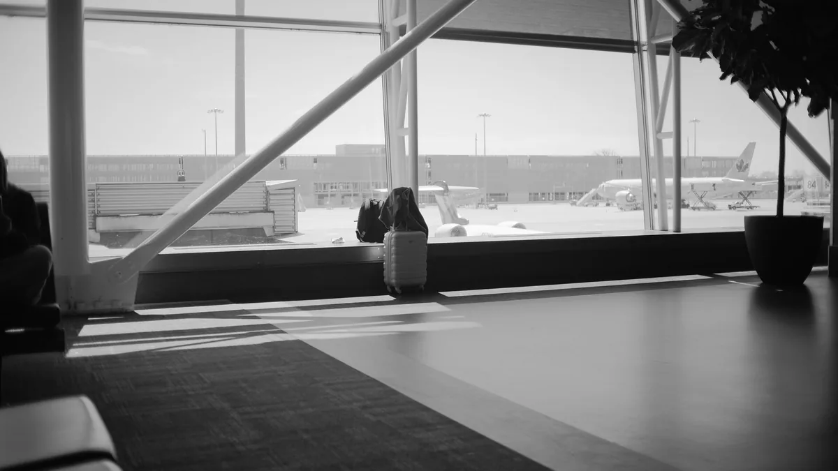 Black and white airport lounge with a single suitcase by the tall windows and parked aircraft on the apron outside