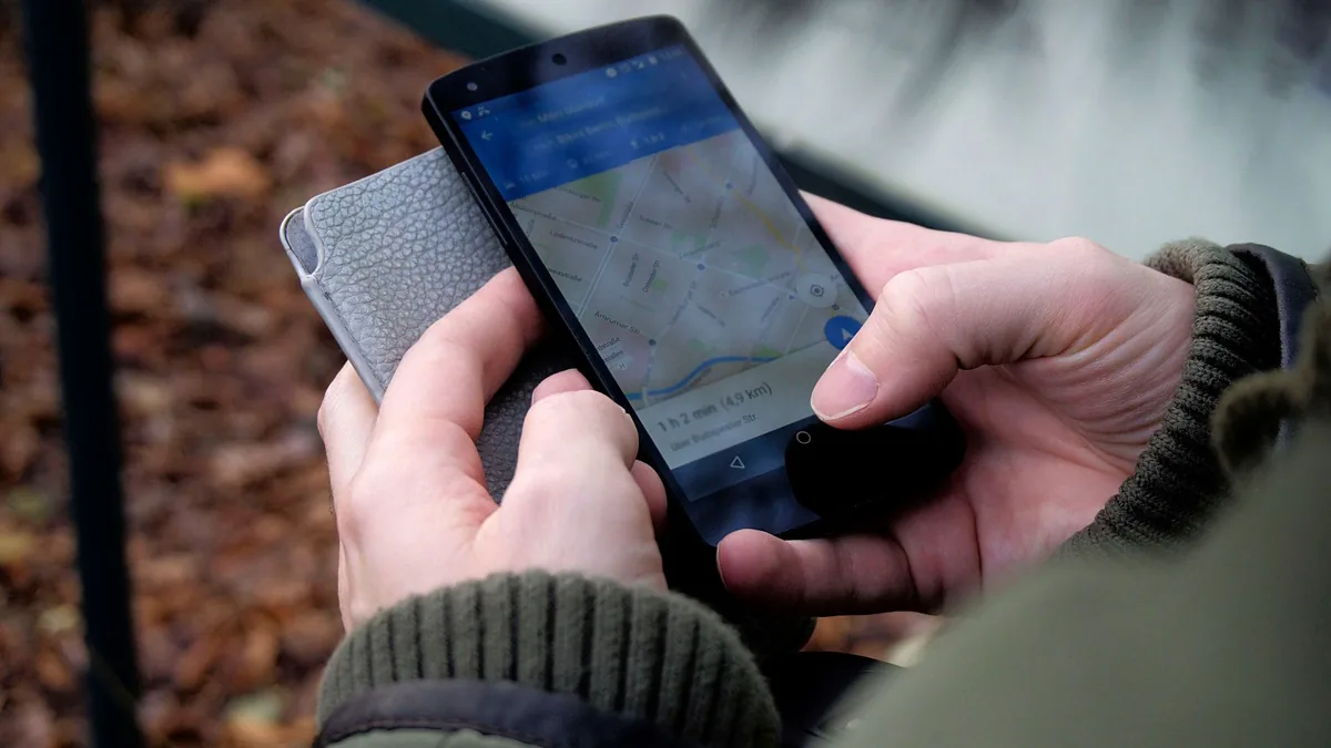 Close-up of two hands holding a smartphone showing a map app, with a grey phone case and autumn leaves behind