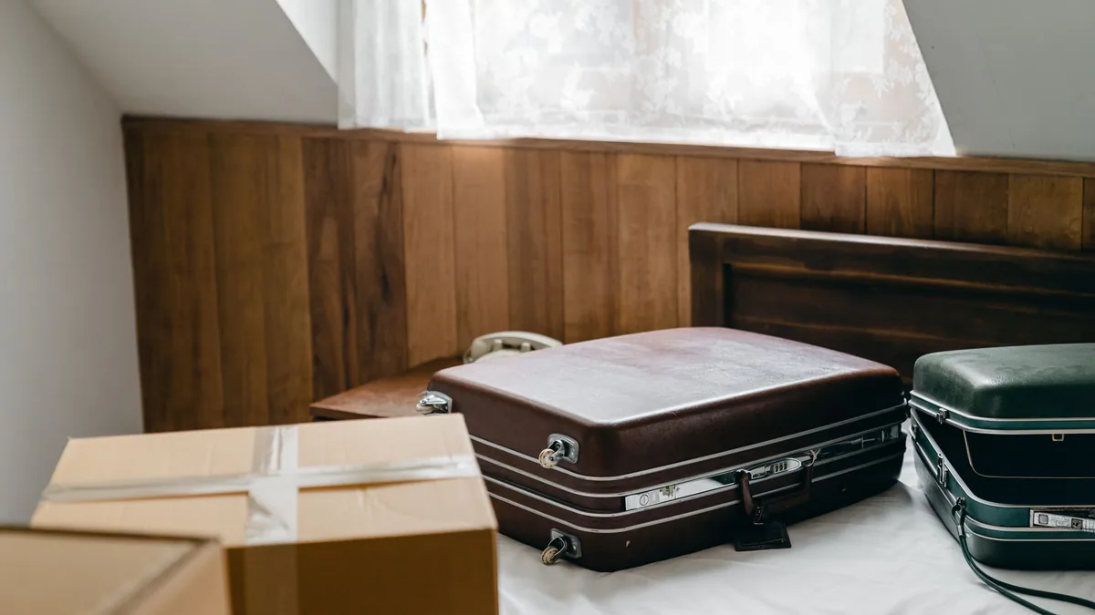 Two hard-shell suitcases and taped cardboard boxes packed on a bed, ready to move to another home