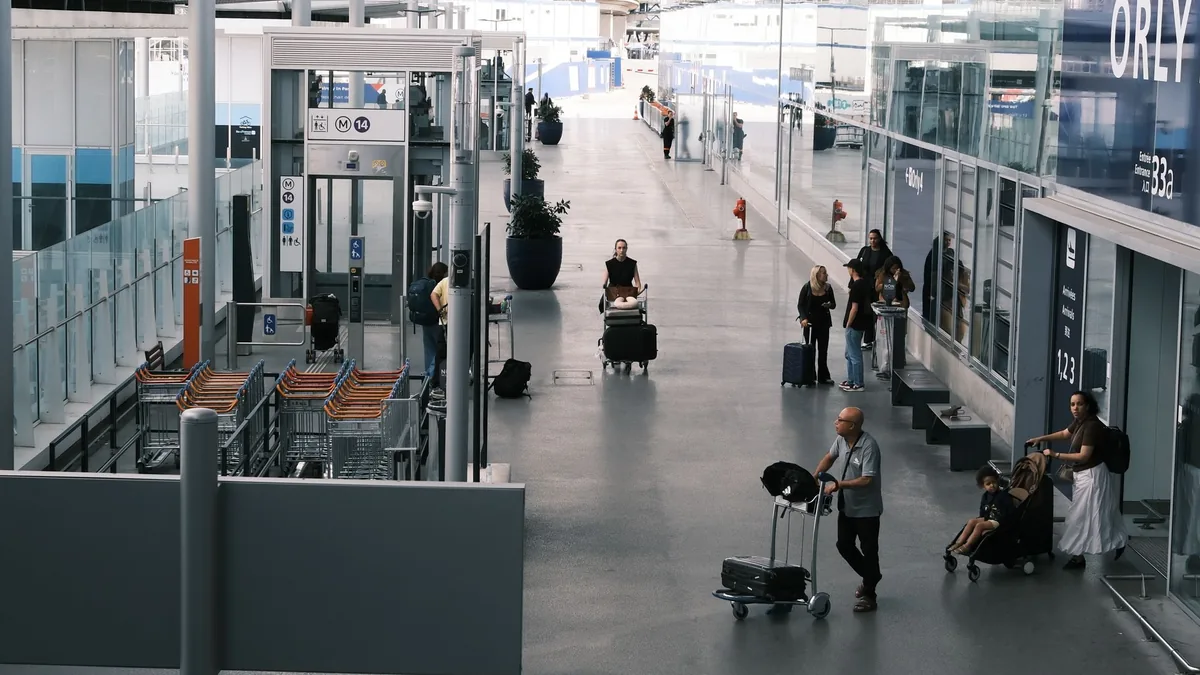 Travellers with luggage trolleys and suitcases walking along a bright airport terminal corridor