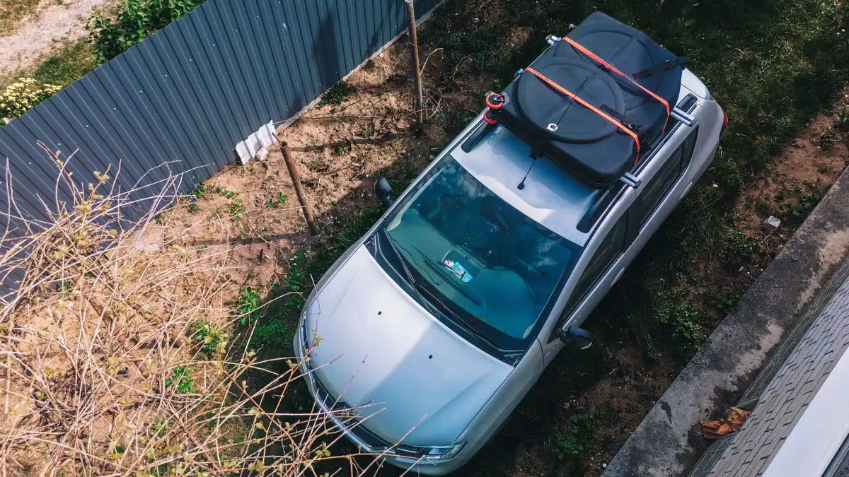 Aerial view of a parked silver hatchback with a strapped soft cargo bag on its roof, showing a car loaded past its boot space