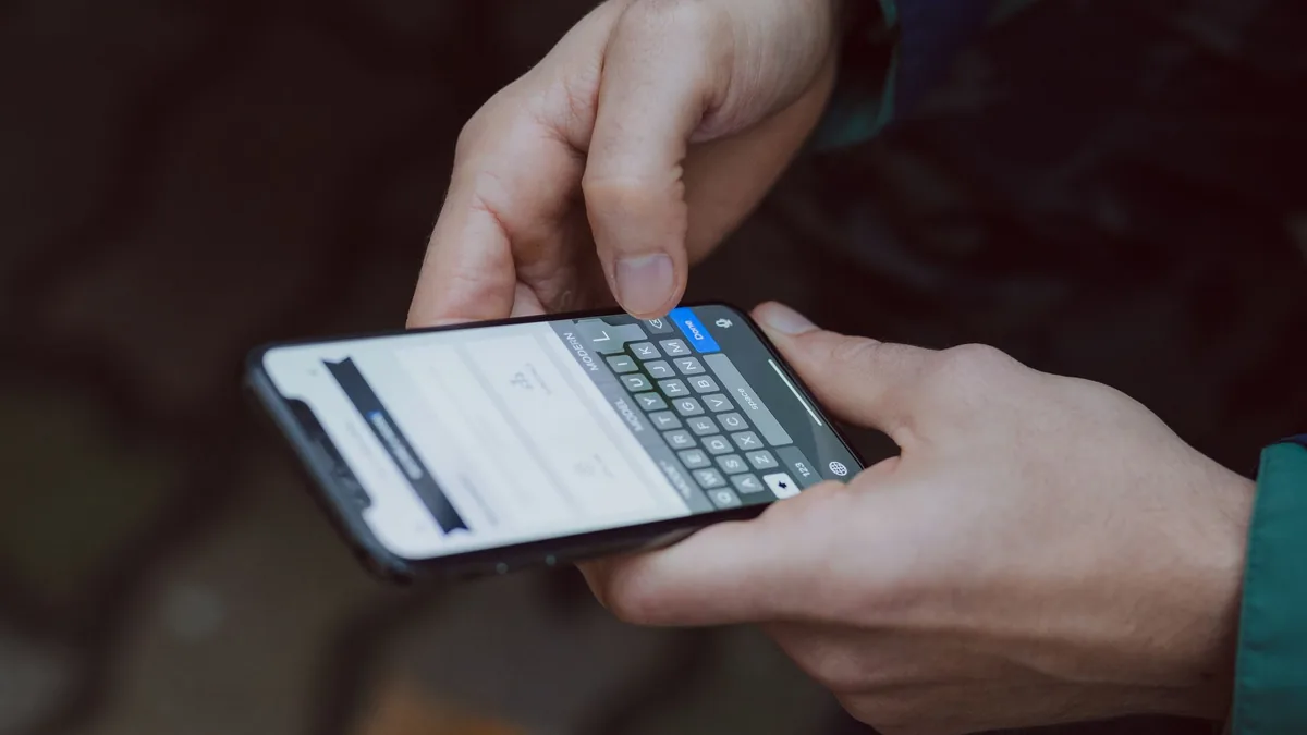 Close-up of two hands typing a message on a smartphone keyboard, face not shown, against a dark background