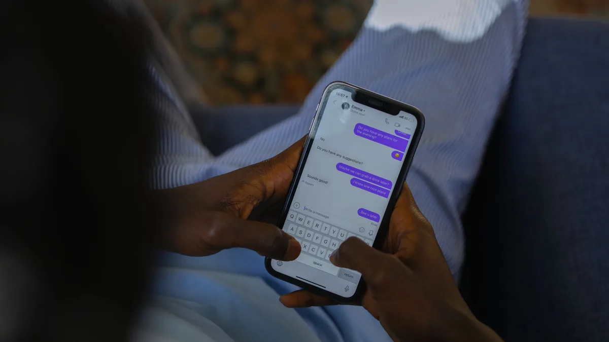 Close-up of two hands holding a smartphone with a chat conversation open, message bubbles on screen, indoors on a sofa