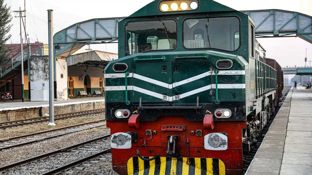 Green and white diesel locomotive standing beside a station platform under a footbridge, with tracks alongside