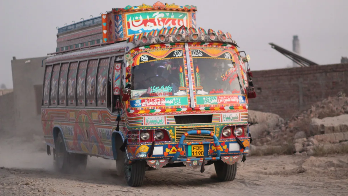 Brightly painted Pakistani passenger bus with truck-art decoration driving along a dusty roadside in Punjab