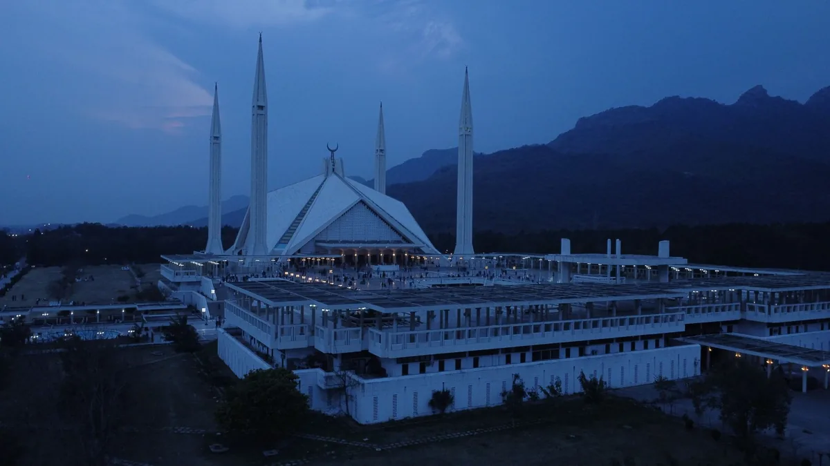 Faisal Mosque in Islamabad at blue-hour twilight, its white minarets set against the dark Margalla Hills