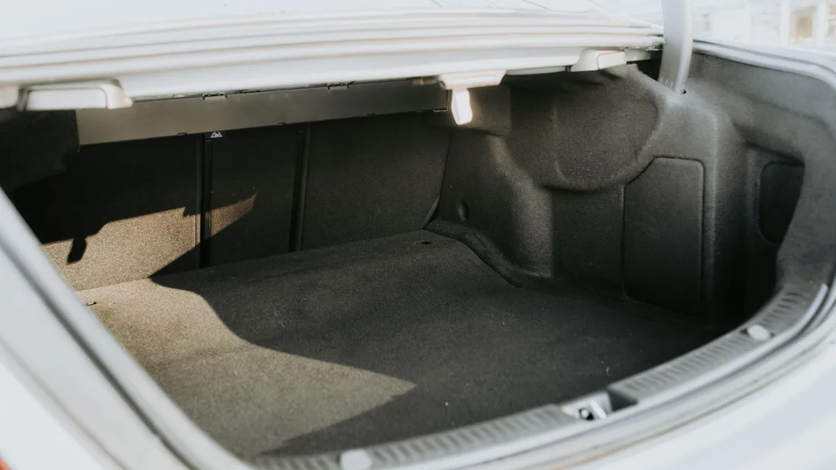 Empty boot of a white saloon car with the lid open, showing the carpeted luggage space in bright sunlight