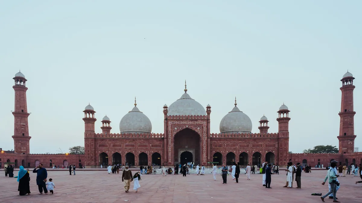 Badshahi Mosque in Lahore seen across its wide red sandstone courtyard, with visitors walking in the early evening