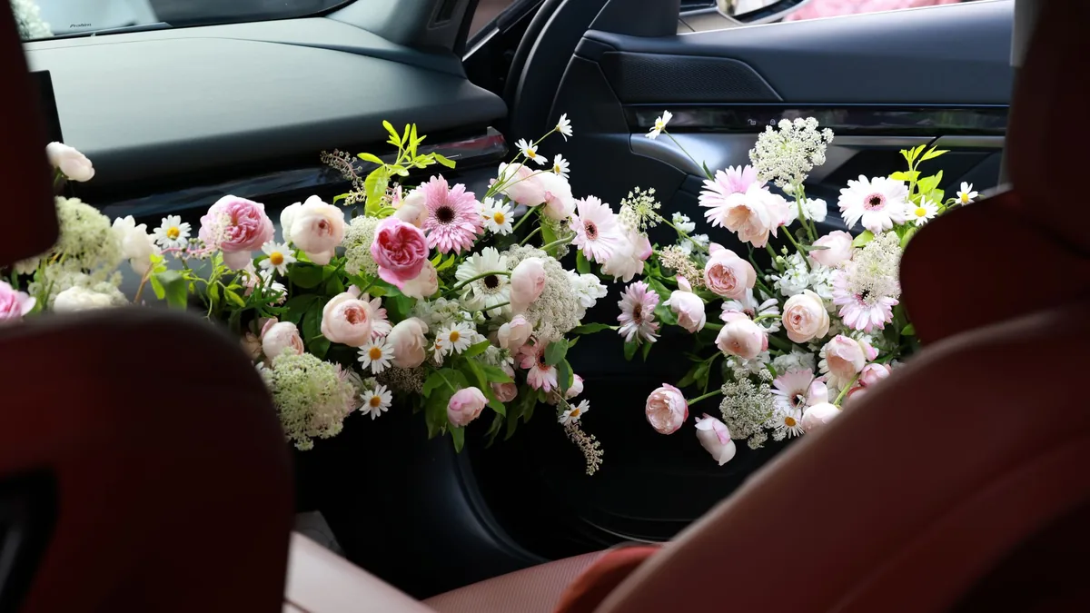 Pink and white flower arrangement laid across the rear seat of a car with dark leather interior, ready for a wedding