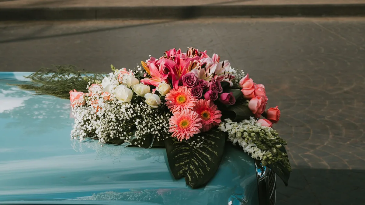 Close-up of a bouquet of pink gerberas, roses and white flowers fixed to the bonnet of a teal car