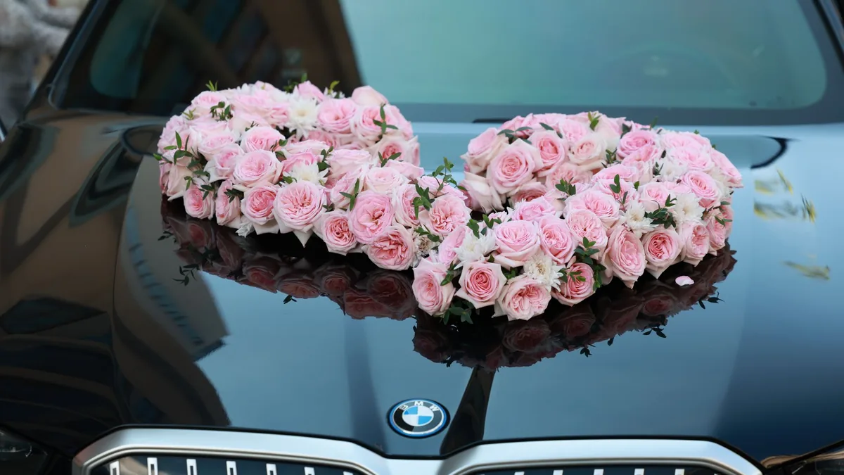 Heart-shaped arrangement of pink roses on the bonnet of a dark car, close-up above the front grille