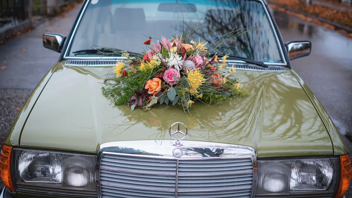 Olive green classic Mercedes saloon with a bright bouquet of roses and wedding flowers on its bonnet