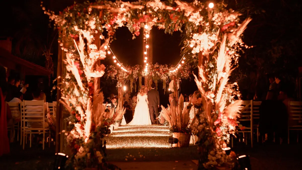 Wedding stage at night framed by an illuminated floral arch with warm string lights and rows of guest seating
