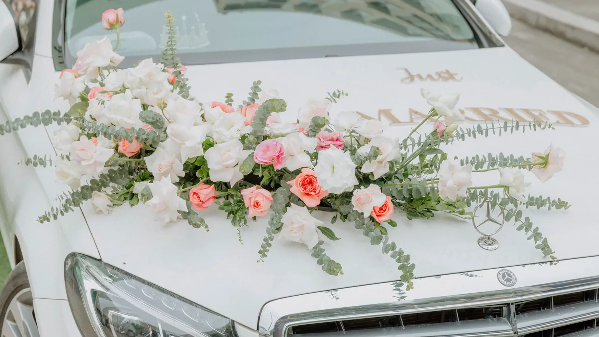 Close-up of a white car bonnet decorated with a spray of pink and white roses and trailing greenery for a wedding