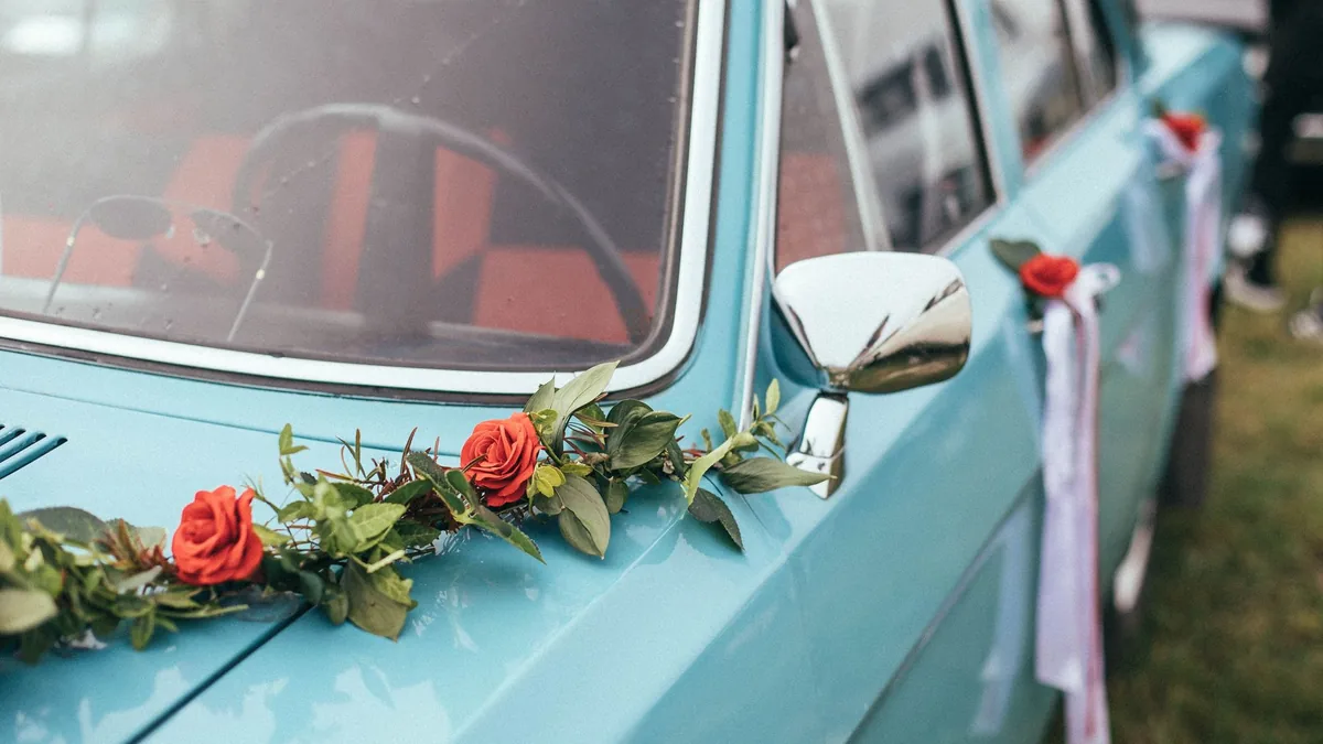 Close-up of a pale blue classic car decorated with red roses, greenery and white ribbons along its side for a wedding