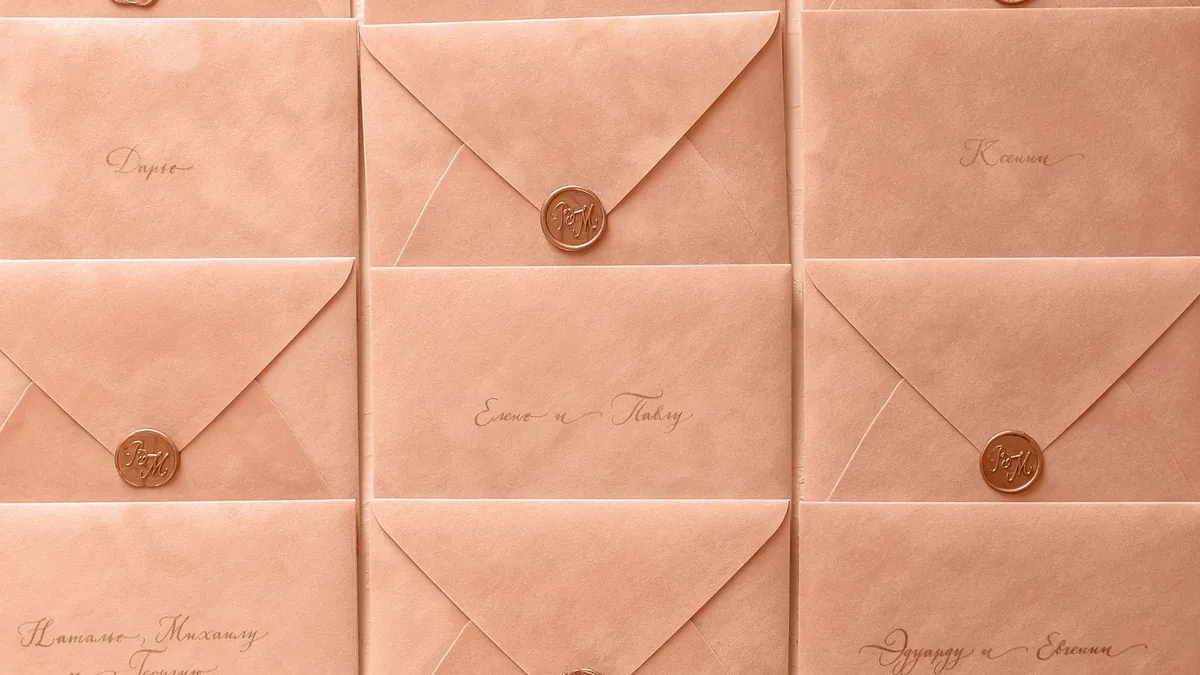 Rows of peach wedding invitation envelopes closed with bronze wax seals, laid out flat and ready to send