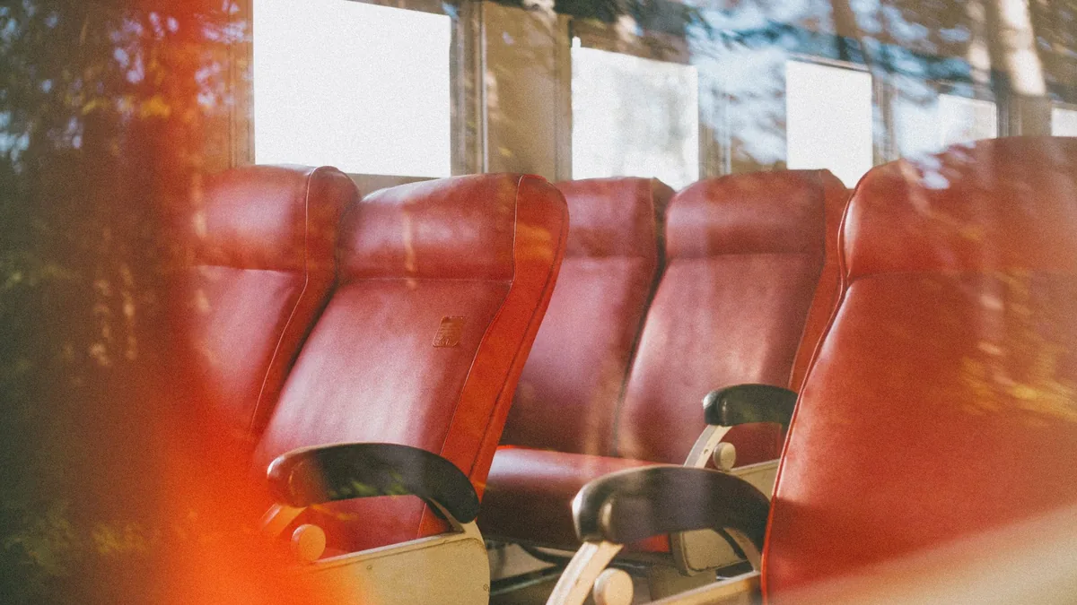 Rows of empty red passenger seats with armrests inside a small bus, lit by soft daylight through the windows