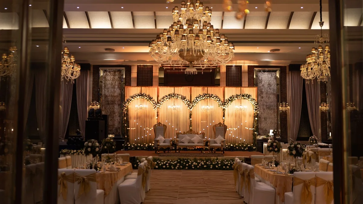 Empty banquet hall set for a wedding reception, with chandeliers, draped tables and a lit stage at the far end