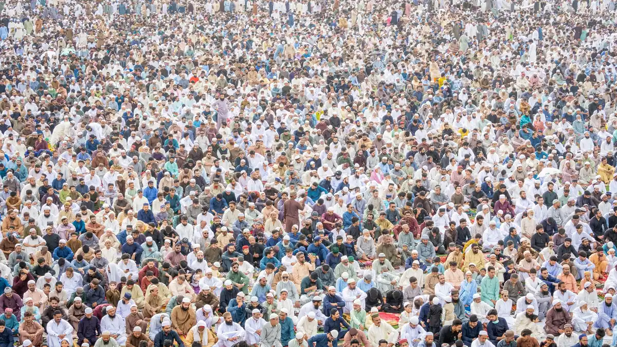 A vast crowd of men in white prayer caps and shalwar kameez seated together at a large outdoor religious gathering