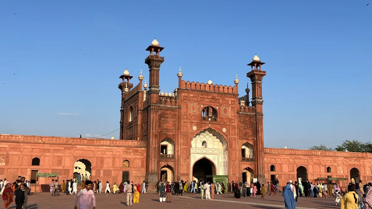 Visitors walking across the forecourt towards the red sandstone gateway of Badshahi Mosque in Lahore under a clear blue sky
