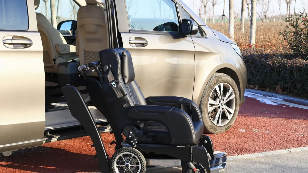 Silver people carrier with its sliding side door open and a swivel transfer seat lowered onto a wheeled wheelchair base beside it