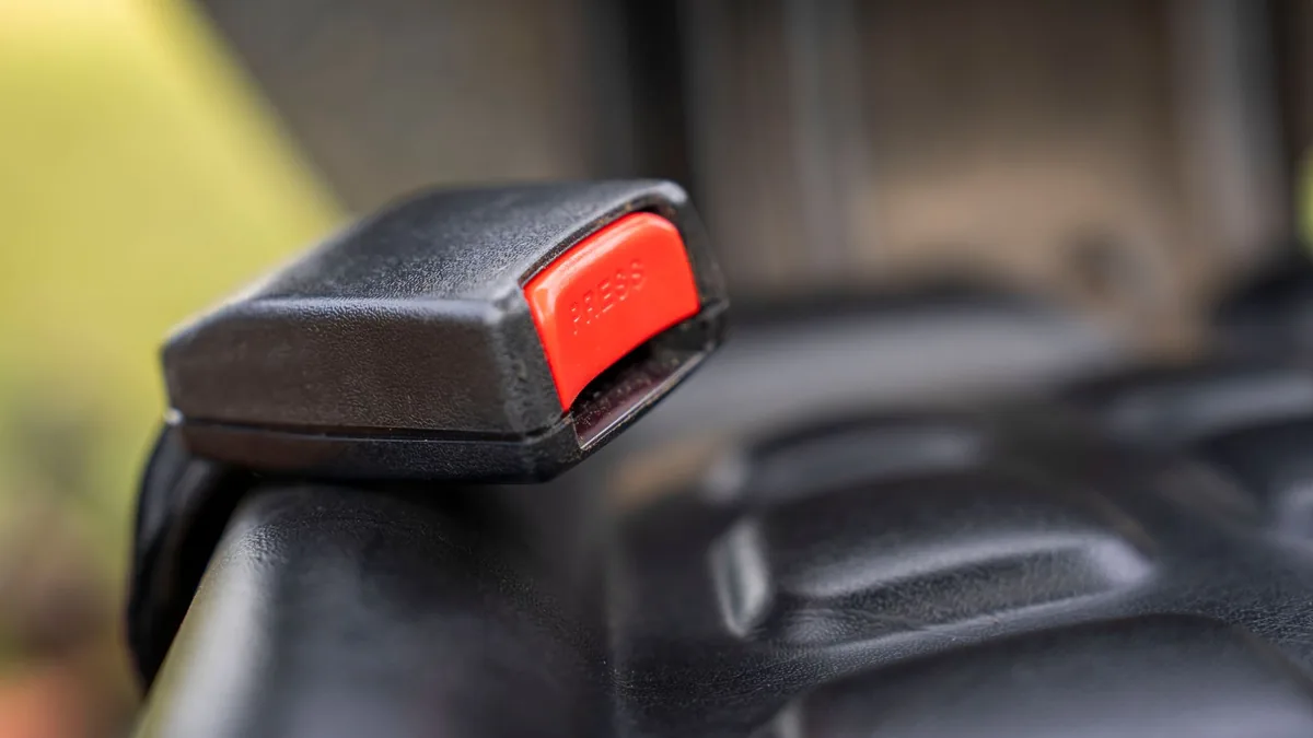 Close-up of a black car seat belt buckle with a red release button beside a dark vehicle seat