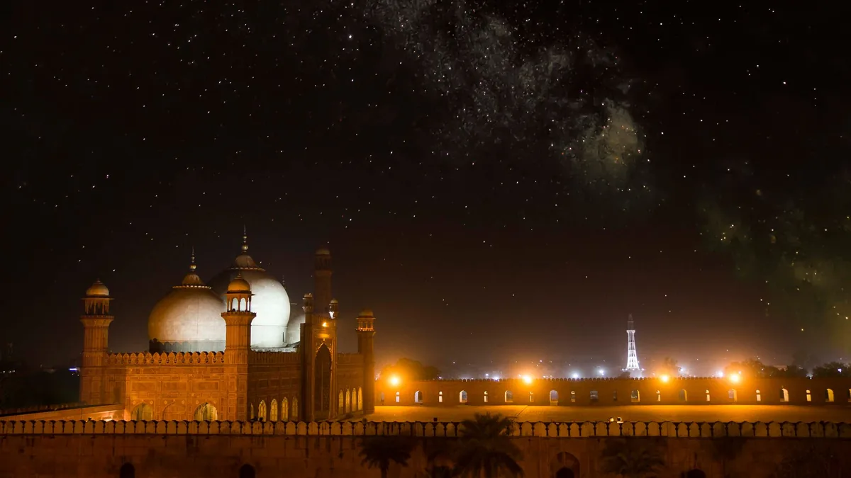 Badshahi Mosque in Lahore lit up at night under a starry sky, with warm lights along the walls below