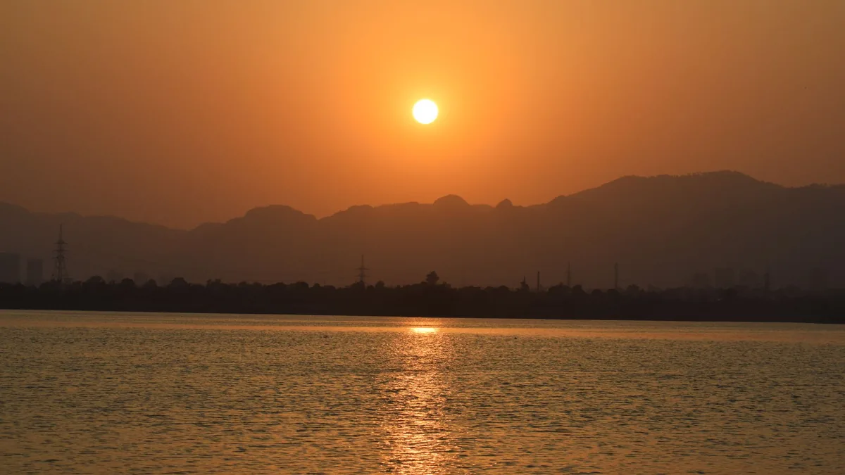 Orange sun setting over calm lake water, with a hazy line of hills along the far shore