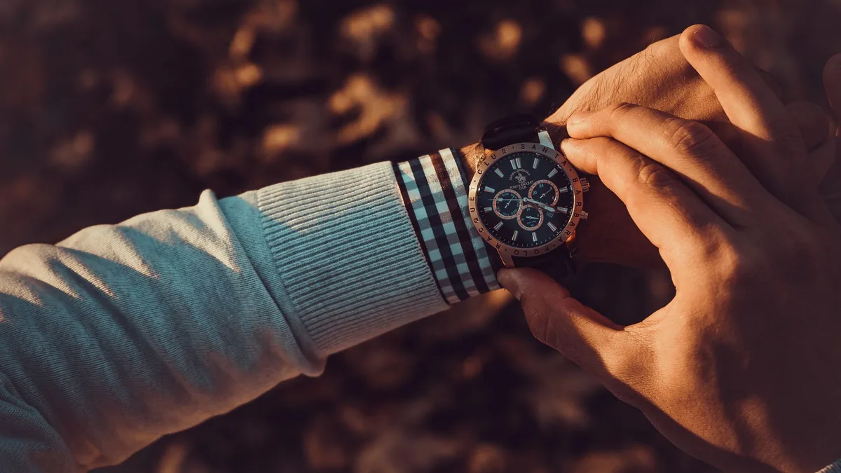Close-up of a hand adjusting an analog chronograph wristwatch on a shirt-cuffed wrist, warm blurred background