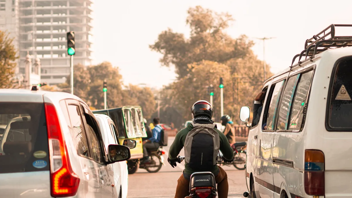 Cars, a van and a motorcyclist waiting at a traffic signal on a busy city road in Lahore on a hazy day