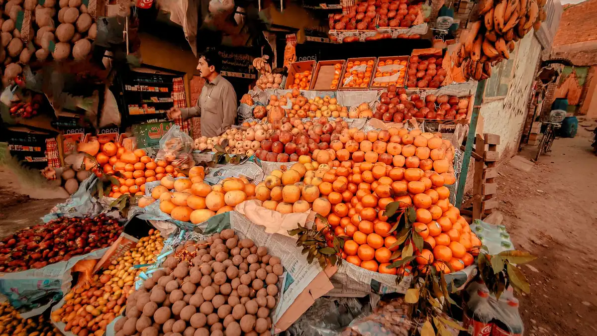 Market stall piled with oranges, dates, dried fruit and bananas under a canopy at an outdoor bazaar