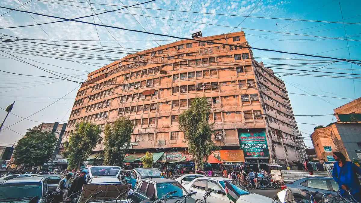 Cars and motorbikes parked along a busy street beneath a tall salmon-coloured apartment block under a blue sky