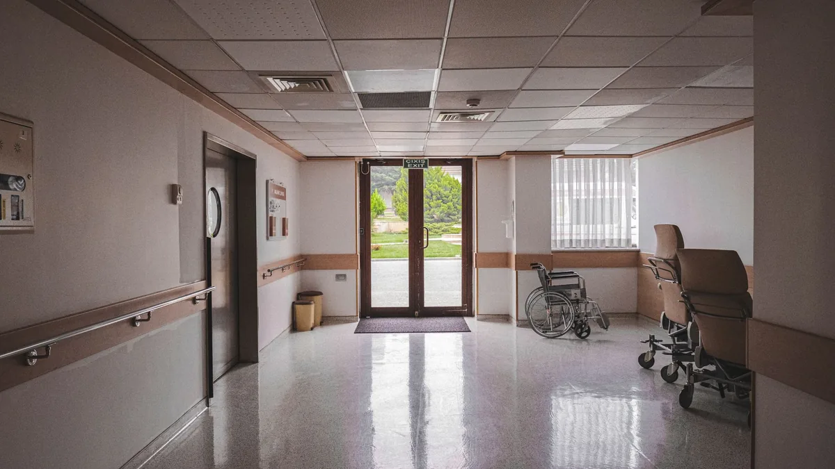 Quiet hospital corridor with polished floor, handrails and parked wheelchairs near glass doors leading outside