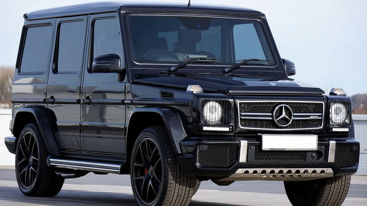 Black Mercedes-Benz G-Class SUV with black alloy wheels parked on a paved lot, front three-quarter view