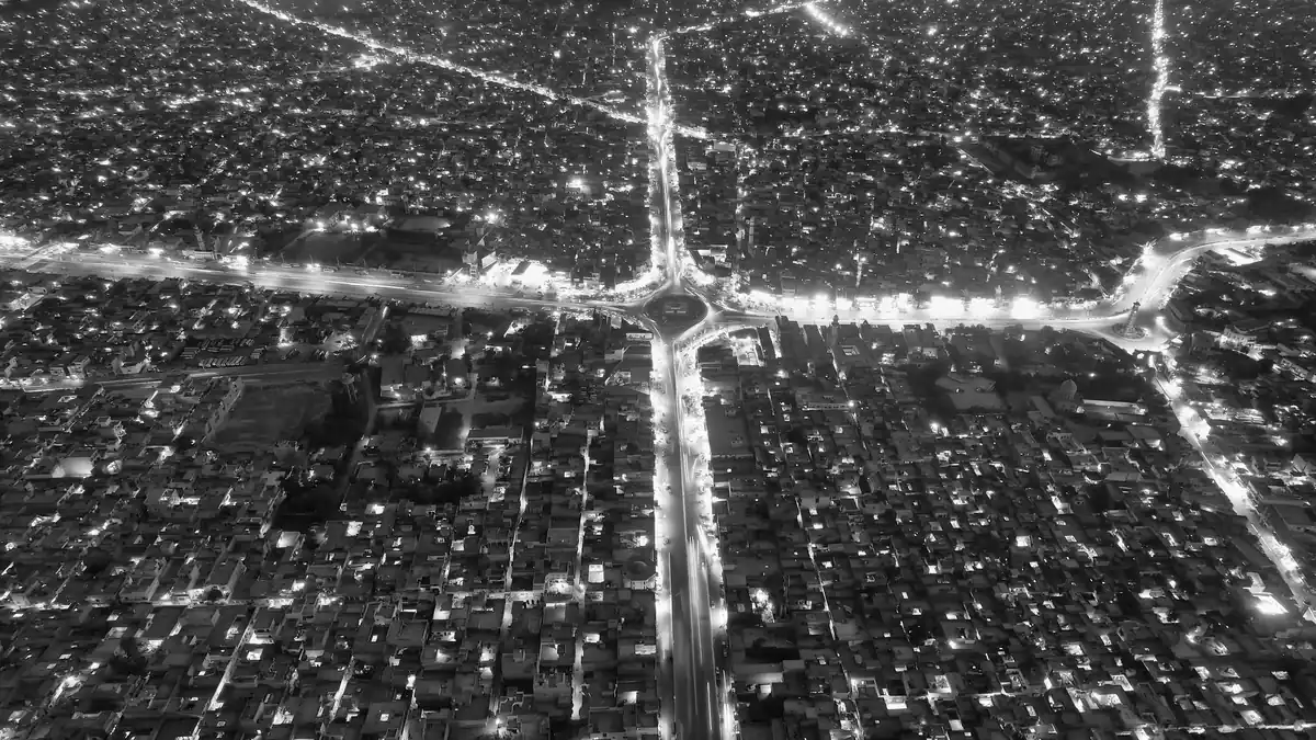 Black-and-white aerial night view of a Punjab city with lit main roads meeting at a roundabout among dense housing
