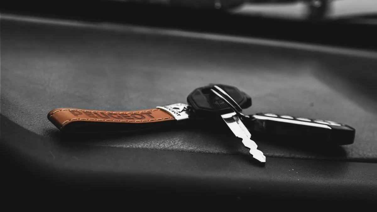 Close-up of a car key with a brown leather keyring resting on a dark car dashboard