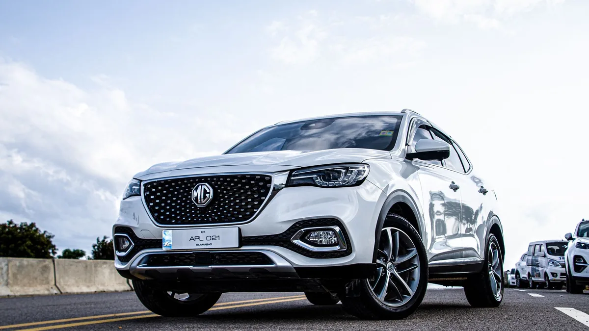 White compact SUV parked on an open road under a cloudy sky, with other cars lined up behind it