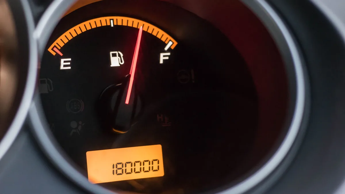 Close-up of a car instrument cluster with the fuel gauge needle at full and an orange backlit odometer reading 180000