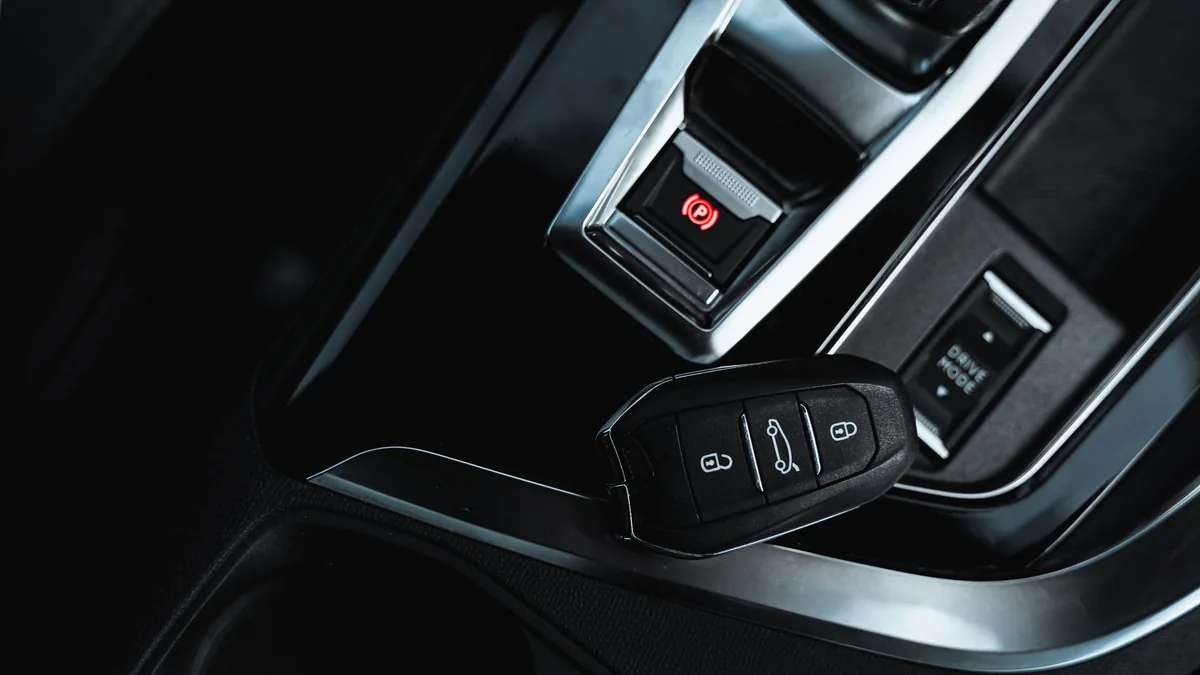 Close-up of a black keyless car key fob resting beside the electronic handbrake and gear controls in a dark car interior