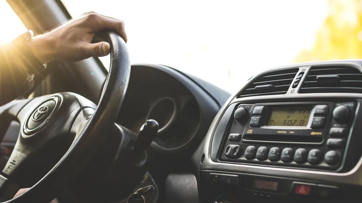 Close-up of a driver's hand on the steering wheel of a right-hand-drive Toyota, with the dashboard and radio visible