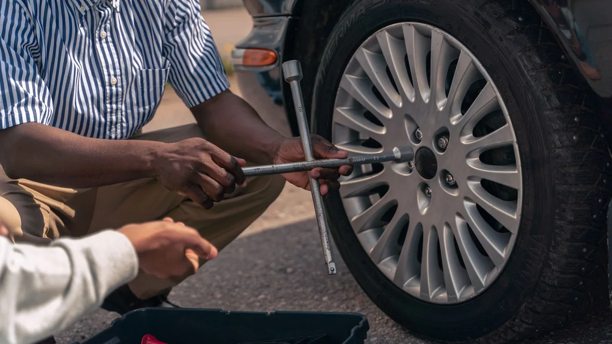 Hands loosening wheel nuts on a car's alloy wheel with a wheel brace, a toolbox open beside the tyre