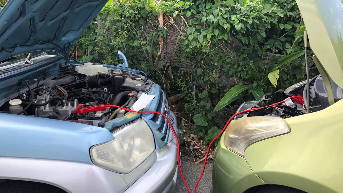 Two cars parked nose to nose with bonnets open, joined by red jumper cables for a battery jump-start