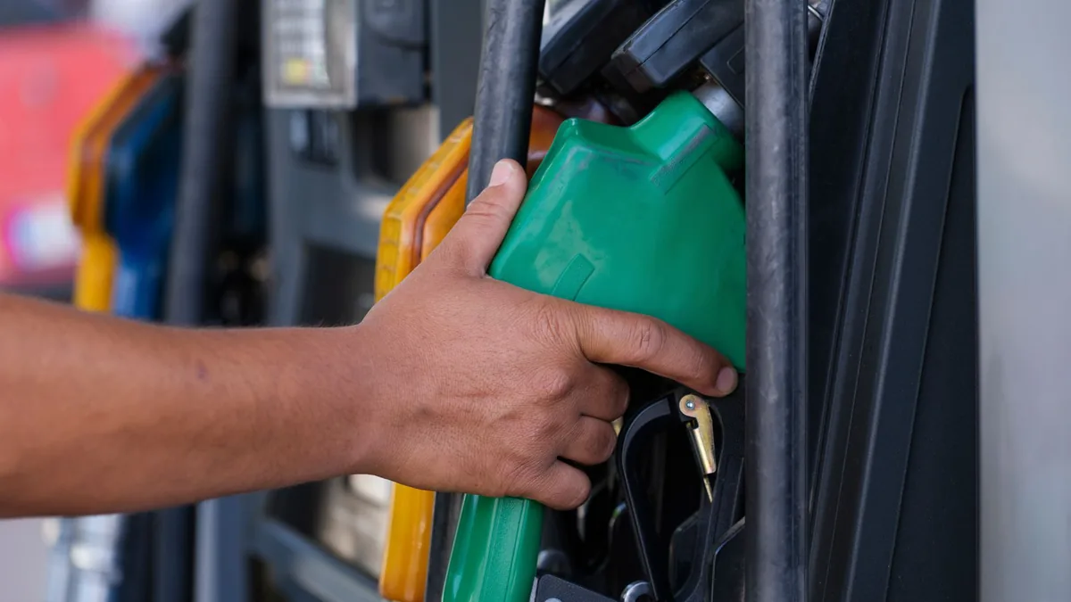 Close-up of a hand holding a green fuel nozzle at a petrol pump dispenser outdoors
